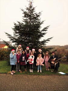 A group of children singing in front of a Christmas tree