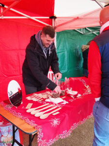 A man arranging products on a table while someone else watches on