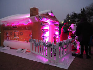 Santa's inflatable grotto at night, lit up with purple lights while Santa and an elf talk to children outside