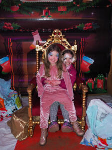 Two young girls sit on a throne made from gold and red, with Christmas presents all around them