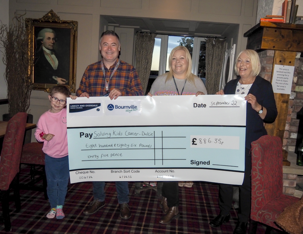 Four people holding a giant novelty cheque, with £886.35 being paid to Solving Kids Cancer - Dulcie