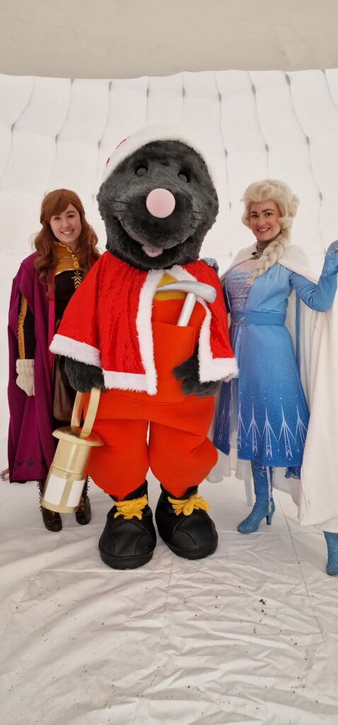 Mawley the mole mascot poses between two women dressed as Disney princesses