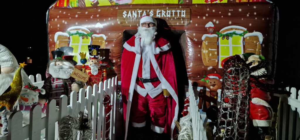 Santa stands in front of an inflatable Santa's grotto