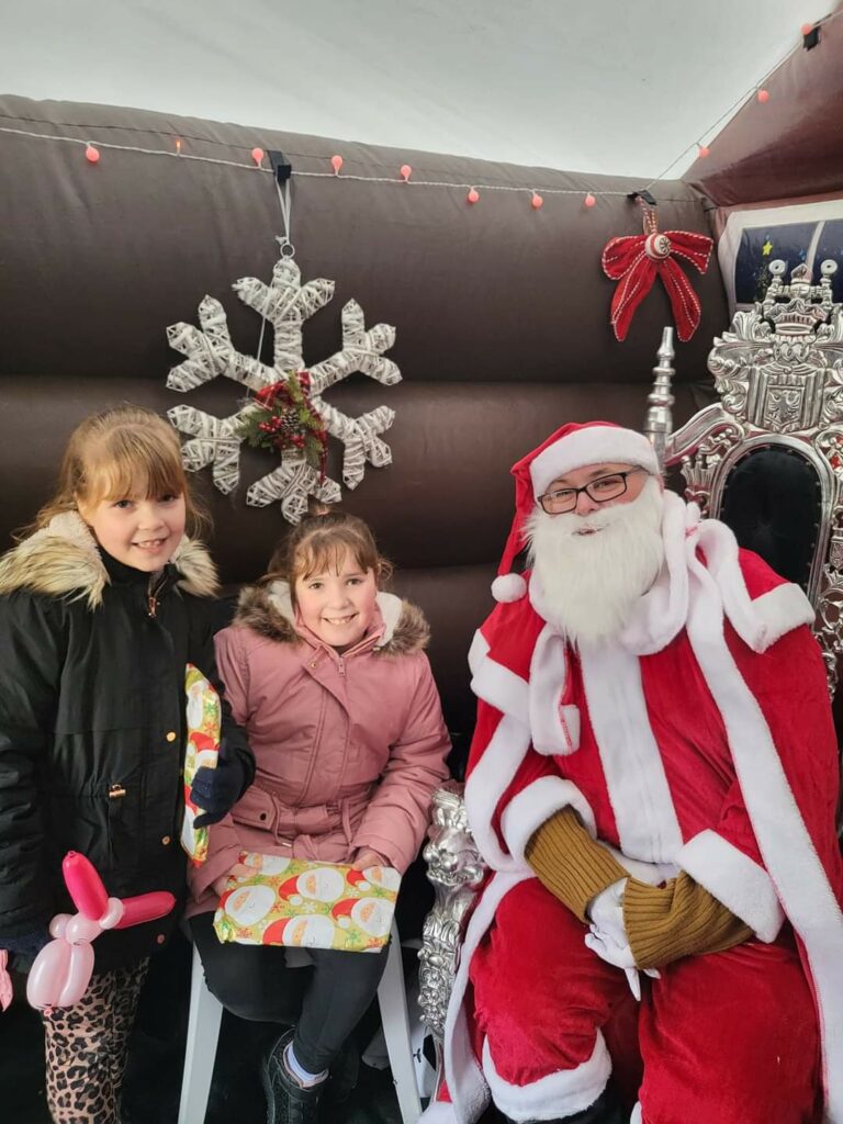 Two children sit inside Santa's grotto with Santa
