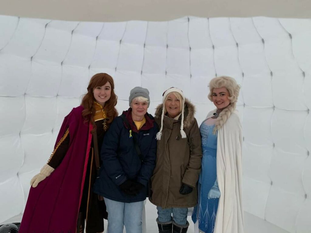Two women in coats stand between two women dressed as Disney princesses, all smiling for the camera