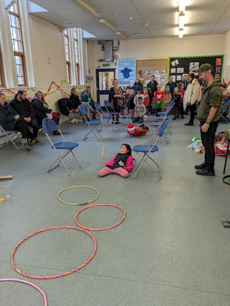 A large group of people stand around a child limboing under a length of string