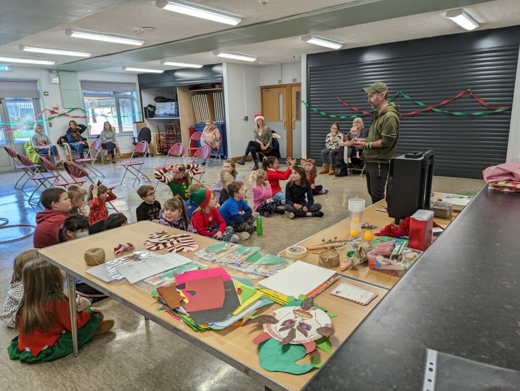 A large group of children sit around a man wearing elf ears