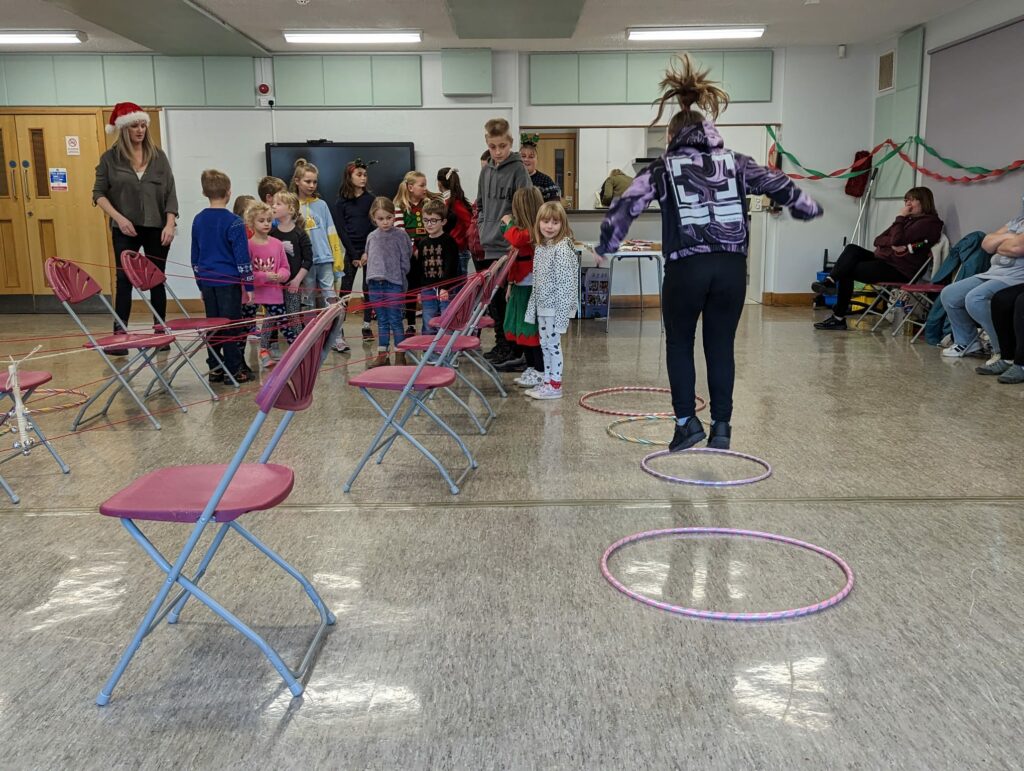 A group watches as a child jumps between hoops laid on the floor