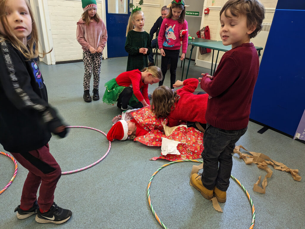 Several children are wrapping another child in wrapping paper