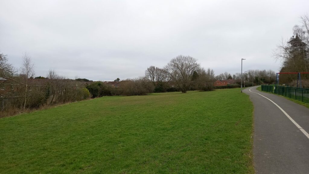A photograph of a footpath with a large grassy area to the left