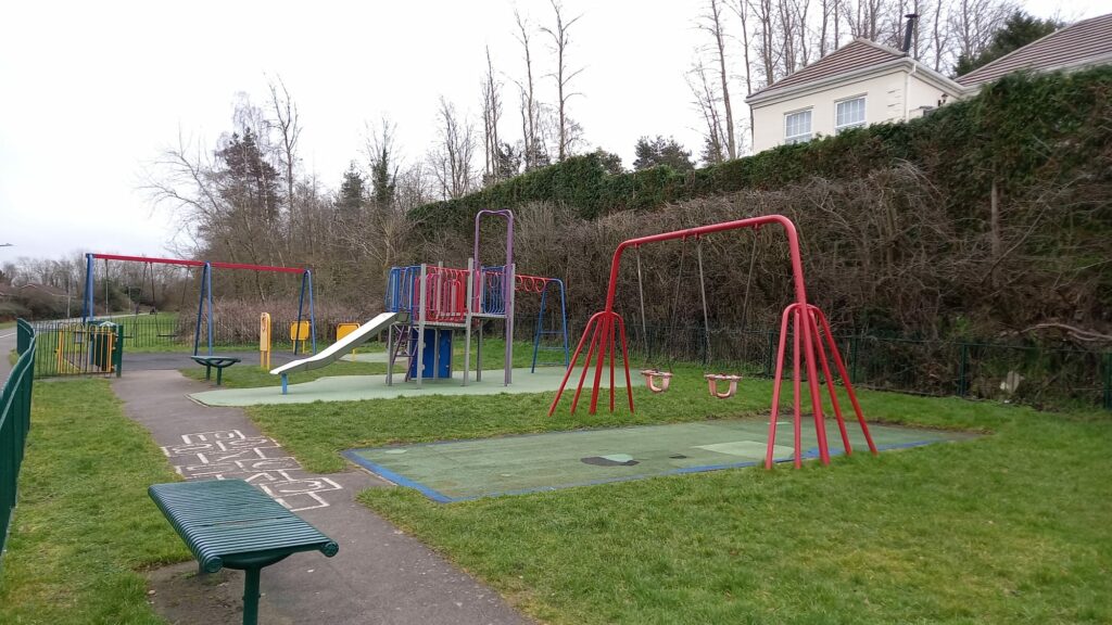 A photograph of a children's play area, with swings, a slide, and a climbing frame