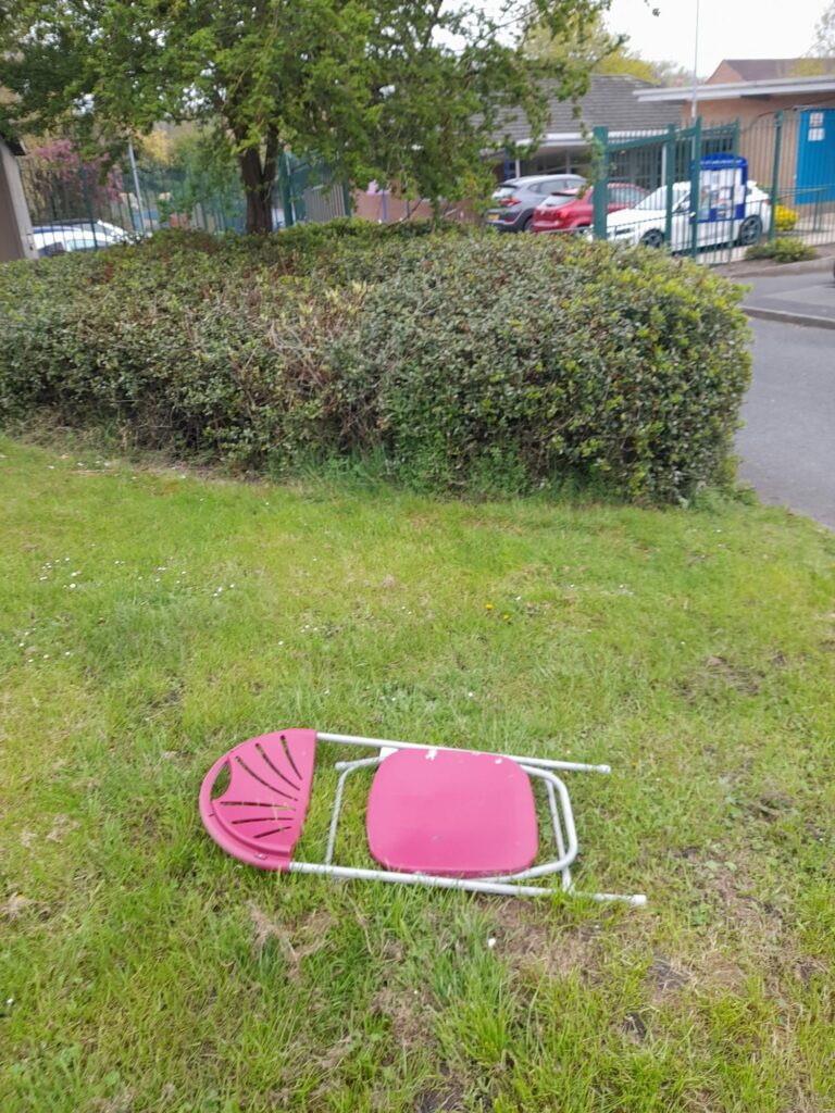 A discarded fold-up chair sitting on a grass verge