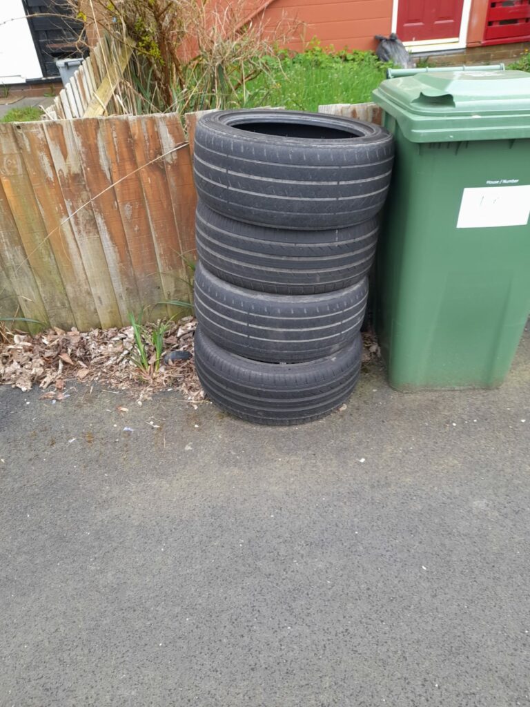 A stack of used tyres propped up against a wheelie bin