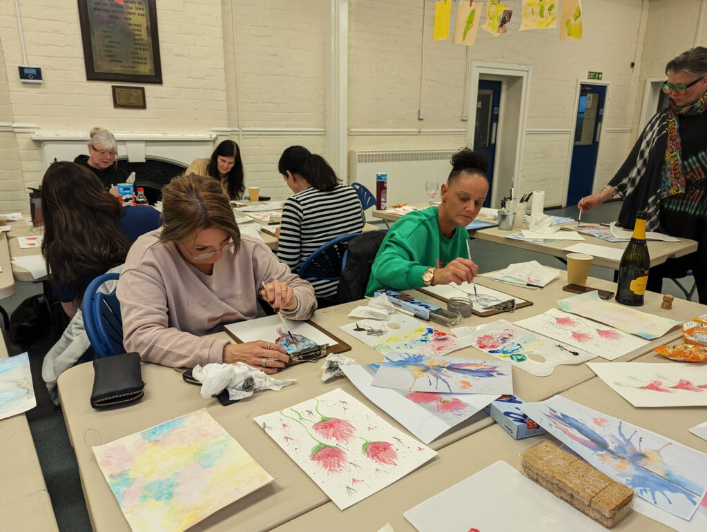 Two people sitting at a table with paintbrushes, painting on paper
