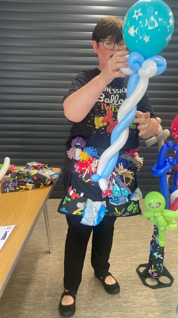 Someone with a T-shirt that reads 'professional balloon twister', twisting two long balloons together