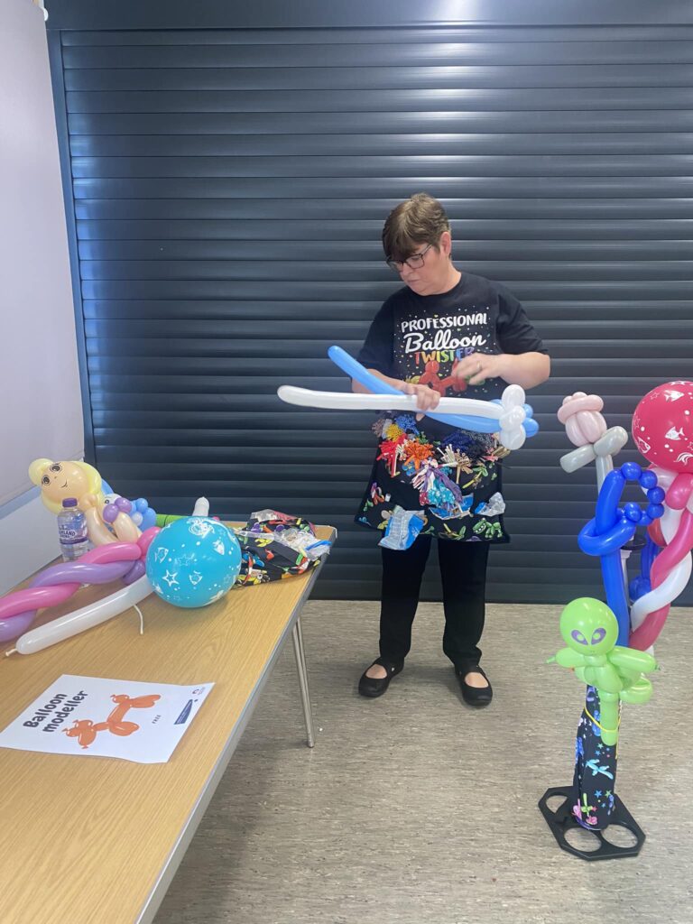 Someone with a T-shirt that reads 'professional balloon twister', twisting two long balloons together