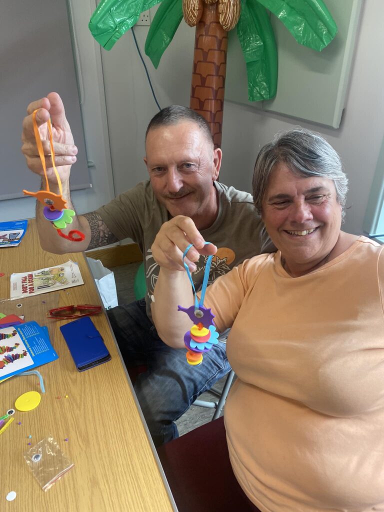 Two people holding up crafts and smiling for the camera