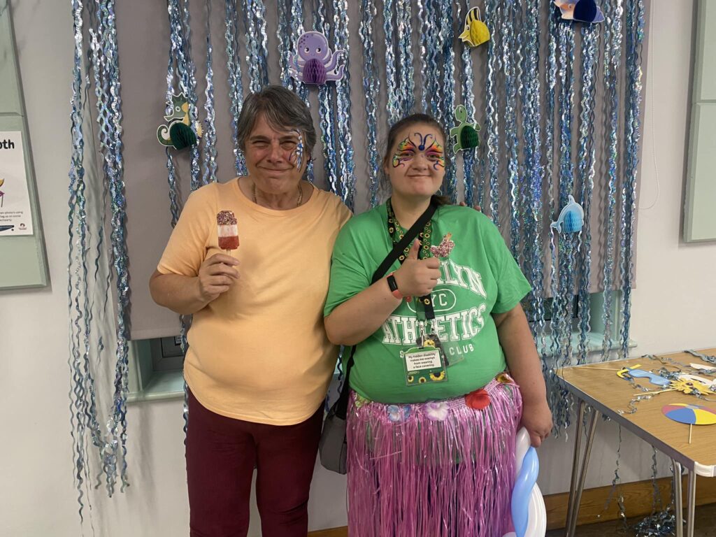 Two people with face paints smiling for the camera. One is wearing a grass skirt, the other holding an ice cream