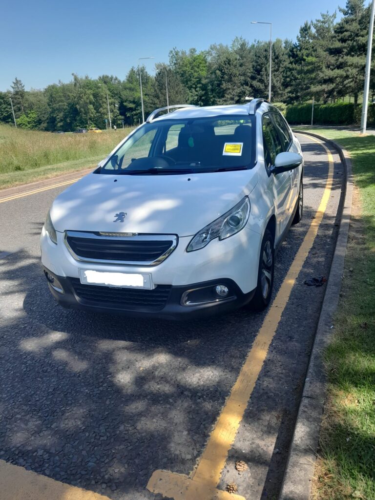 A photograph of an SUV parked on a yellow line. A penalty sticker is attached to the windscreen