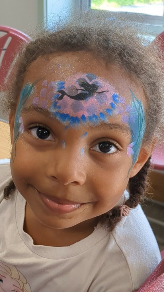 A child with face paints on their forehead smiling for the camera
