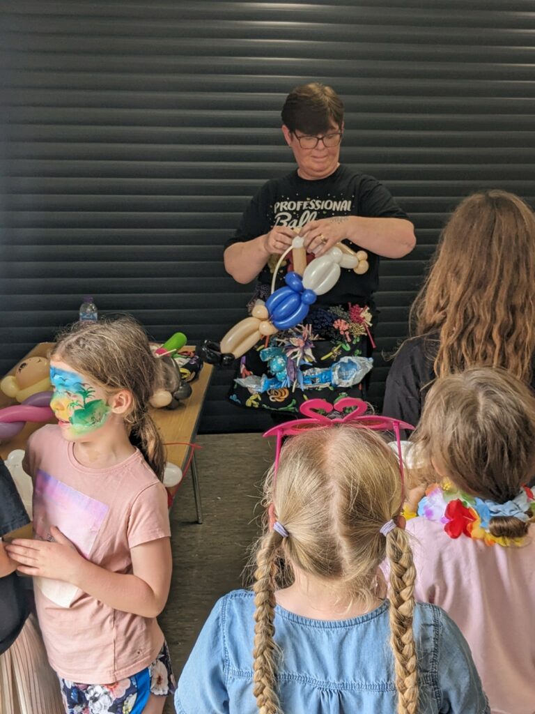 An adult twists several balloons together while a group of children watch