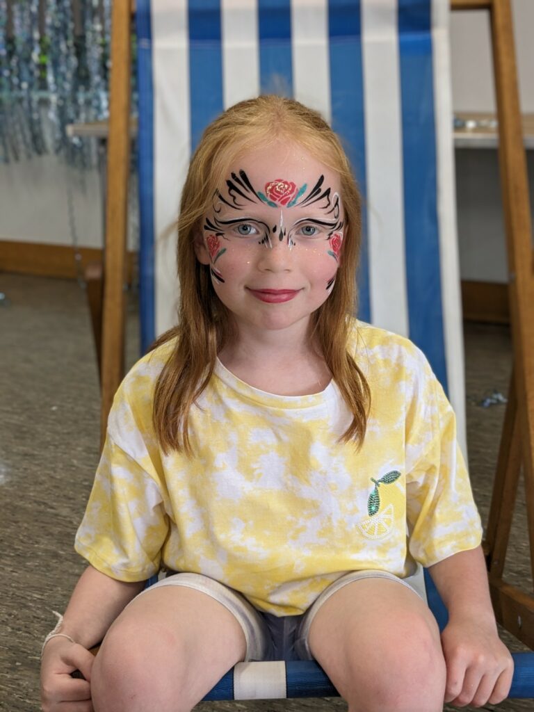 A face-painted child sits in a deck chair