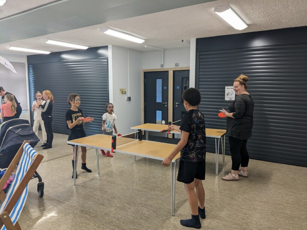 Two table tennis tables, with a group of people playing table tennis